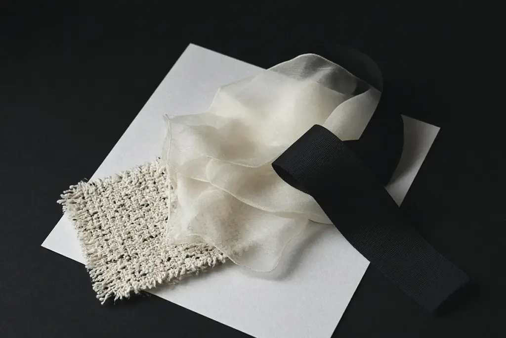 Swatches of cream tweed, sheer fabric and black ribbon fanned out on white paper, a still life inspired by Chanel spring 2027